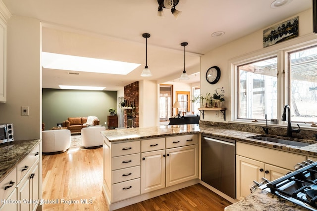 kitchen with light wood-type flooring, a sink, stainless steel dishwasher, a peninsula, and stone counters