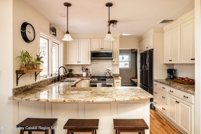 kitchen with visible vents, a sink, light stone counters, stainless steel appliances, and a peninsula