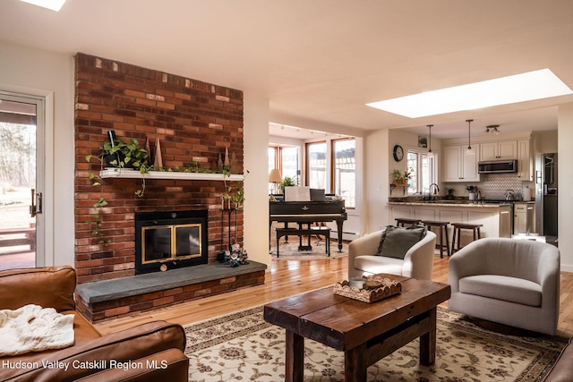 living area with baseboard heating, a brick fireplace, a skylight, and wood finished floors