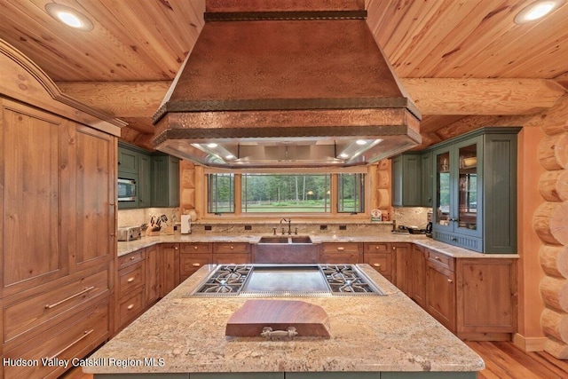 kitchen featuring light wood-type flooring, light stone counters, custom exhaust hood, a center island, and green cabinets