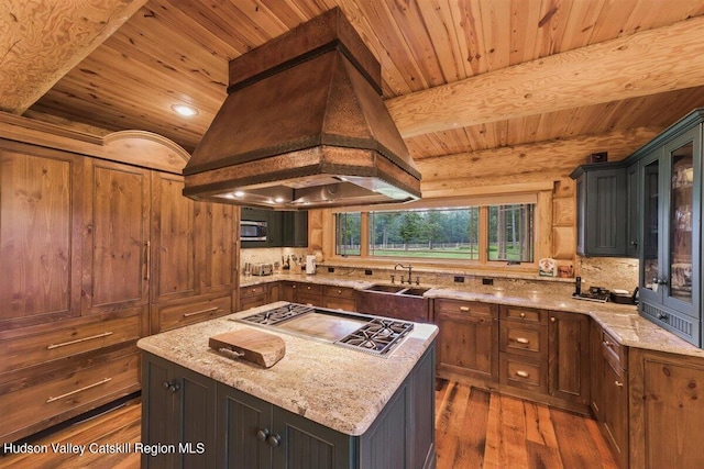 kitchen featuring premium range hood, light stone counters, sink, hardwood / wood-style floors, and a center island