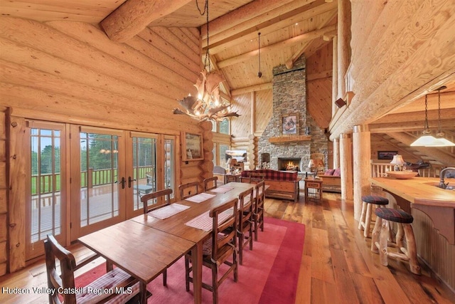 dining area with french doors, wood-type flooring, beam ceiling, high vaulted ceiling, and a stone fireplace