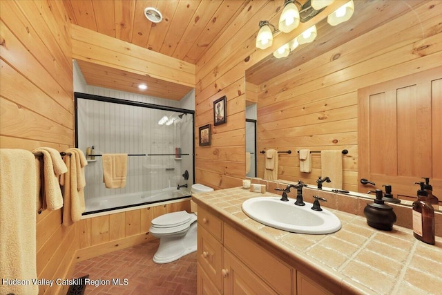 full bathroom with combined bath / shower with glass door, vanity, toilet, and wood walls