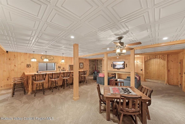 dining area featuring ceiling fan, wood walls, light carpet, and bar area