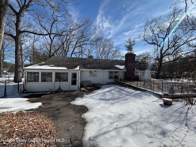 snow covered back of property featuring a chimney, fence, and a sunroom