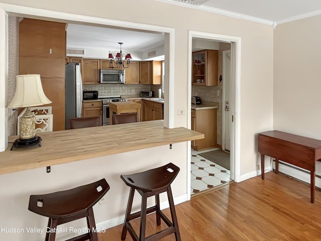 kitchen with crown molding, appliances with stainless steel finishes, a breakfast bar, and brown cabinets