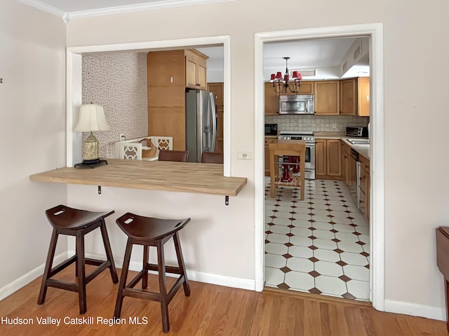 kitchen featuring butcher block counters, appliances with stainless steel finishes, a breakfast bar, ornamental molding, and a chandelier