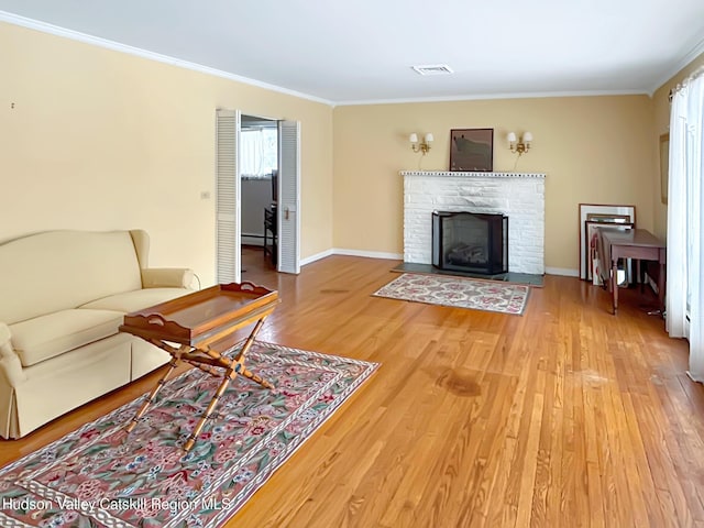 living area featuring a fireplace with flush hearth, wood finished floors, visible vents, baseboards, and ornamental molding