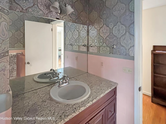 bathroom featuring a wainscoted wall, wood finished floors, vanity, and wallpapered walls