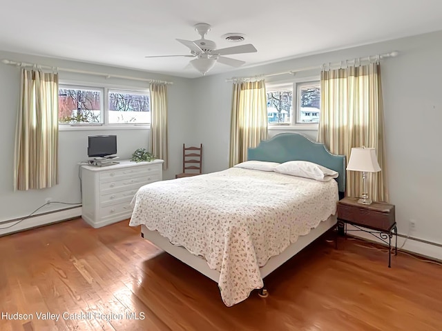 bedroom featuring a baseboard heating unit, a ceiling fan, visible vents, and light wood-style floors