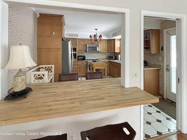 kitchen with a notable chandelier, stainless steel appliances, a peninsula, decorative backsplash, and wallpapered walls