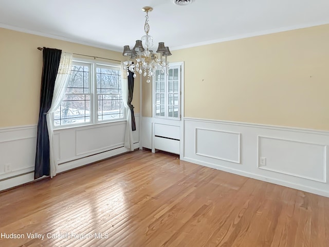 unfurnished dining area featuring a wainscoted wall, baseboard heating, an inviting chandelier, ornamental molding, and wood finished floors