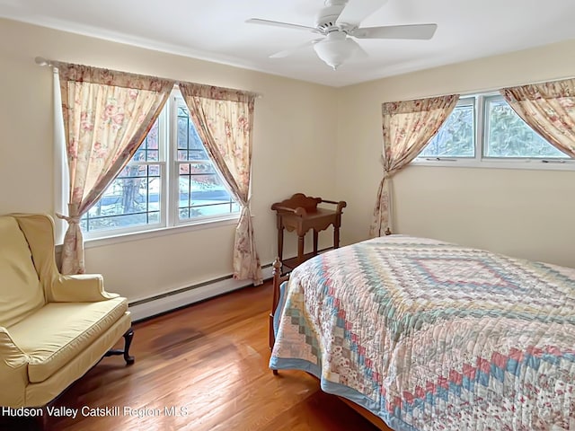 bedroom with a baseboard heating unit, multiple windows, wood finished floors, and a ceiling fan