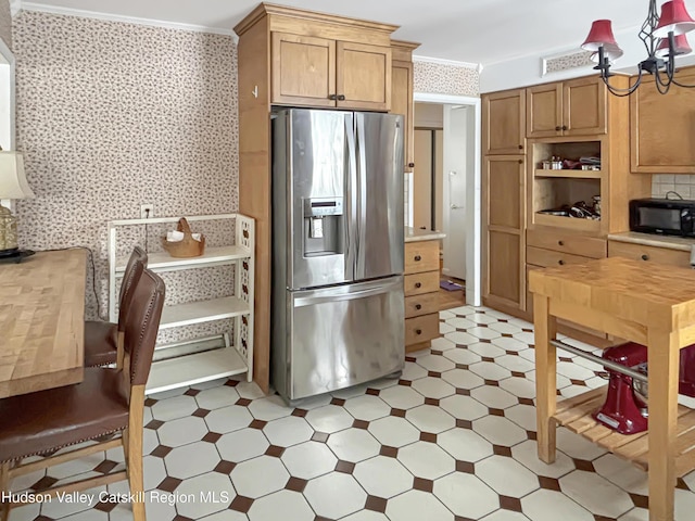 kitchen with wallpapered walls, stainless steel fridge with ice dispenser, ornamental molding, light countertops, and black microwave