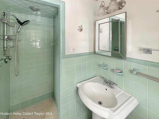 full bathroom featuring wainscoting, tile walls, a sink, and tiled shower