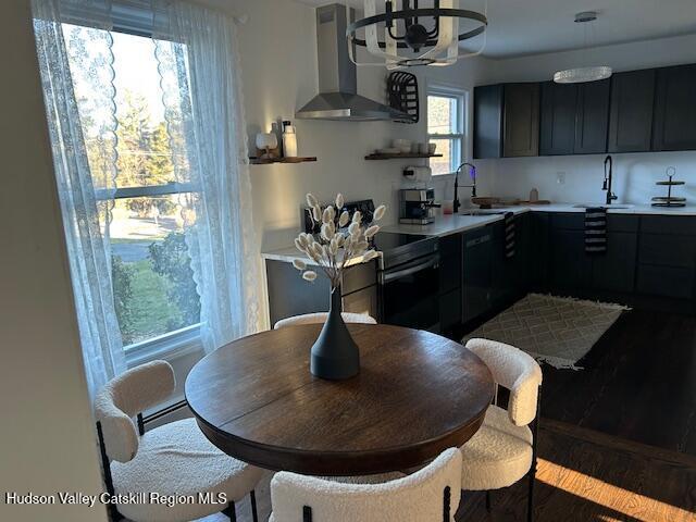 kitchen with wall chimney range hood, hardwood / wood-style floors, sink, and black dishwasher