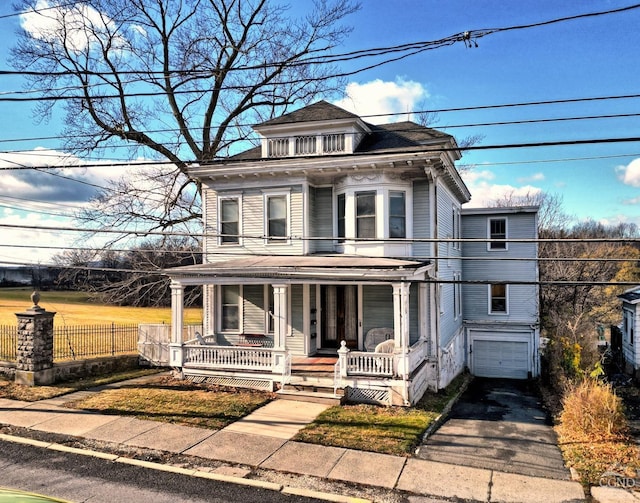 american foursquare style home with covered porch, an attached garage, asphalt driveway, fence, and a shingled roof