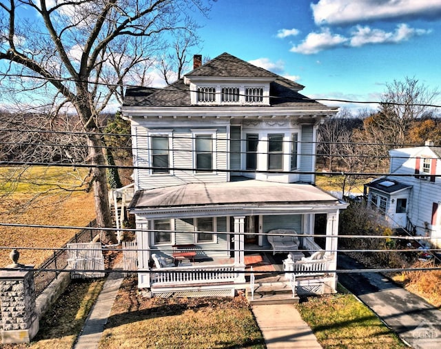 view of front of house with a chimney, fence, covered porch, and a balcony