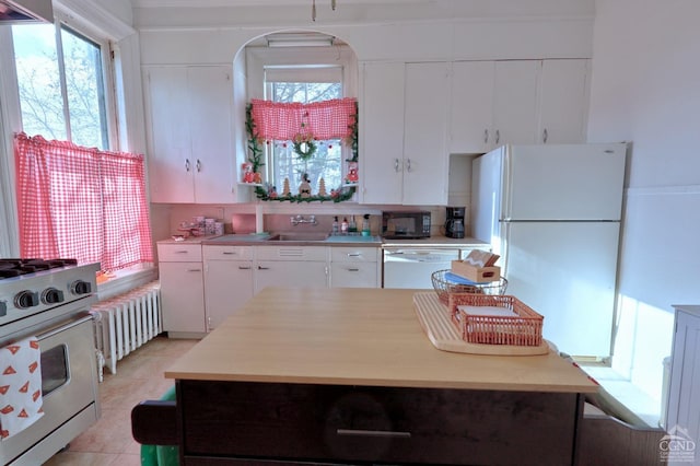 kitchen with radiator heating unit, white appliances, light countertops, white cabinetry, and plenty of natural light