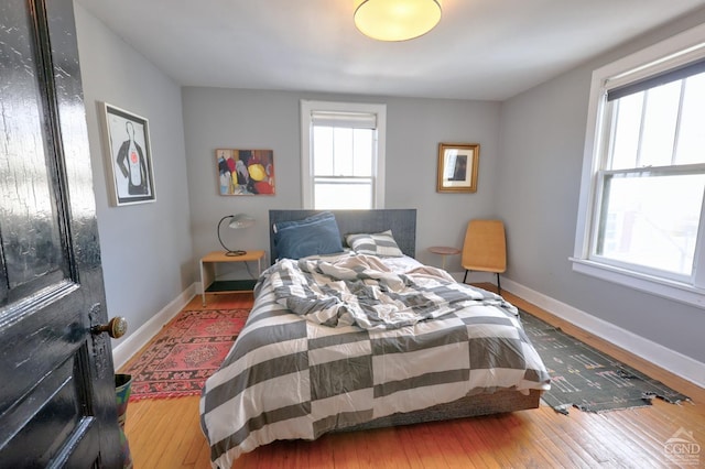 bedroom with multiple windows, hardwood / wood-style flooring, and baseboards