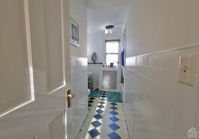 hallway with tile walls, light flooring, and wainscoting