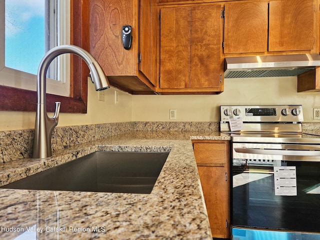 kitchen featuring light stone countertops, exhaust hood, electric stove, and sink