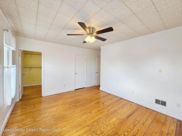 unfurnished bedroom featuring ceiling fan, a spacious closet, crown molding, and light hardwood / wood-style flooring