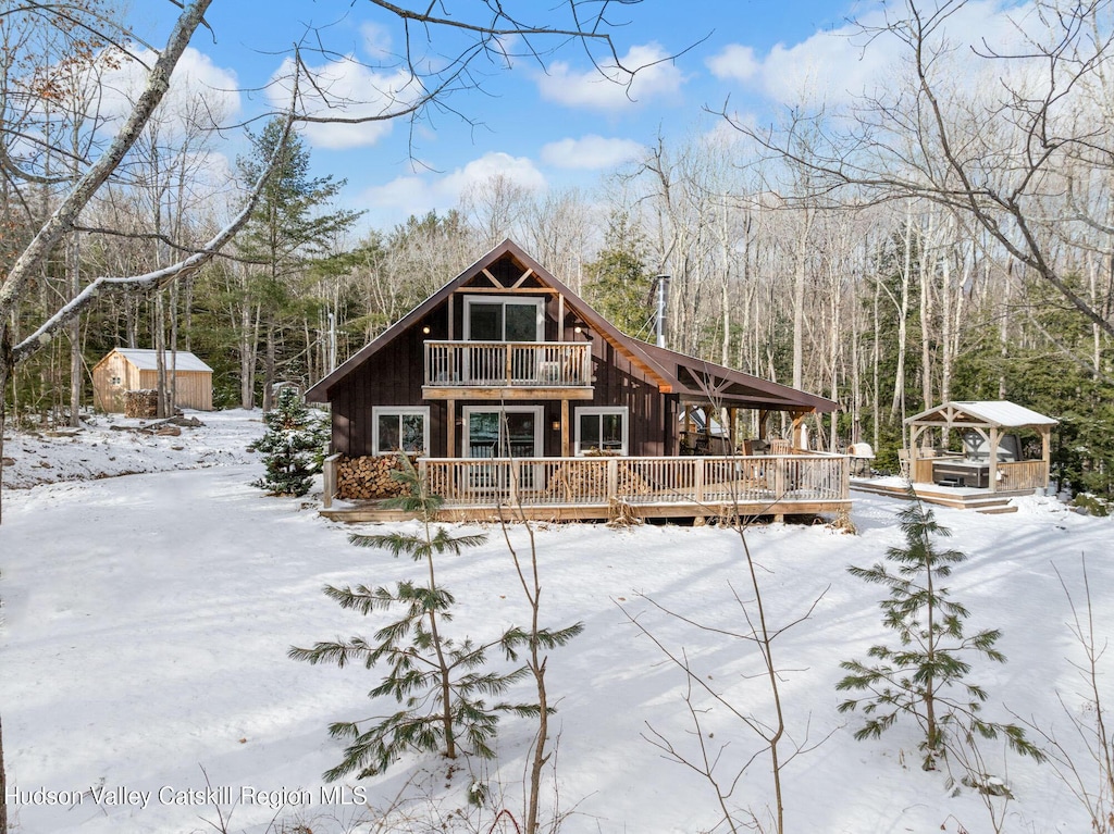 snow covered rear of property featuring a deck and a storage shed