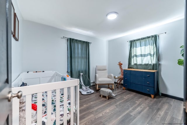 bedroom with a crib, a baseboard heating unit, and wood finished floors