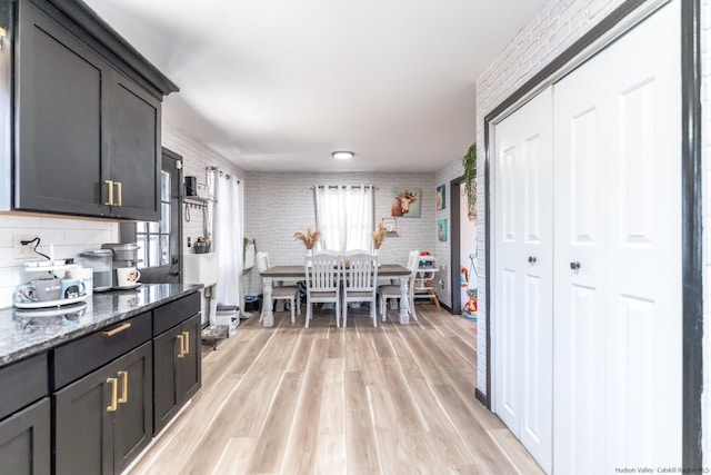 kitchen featuring stone counters, backsplash, light wood-type flooring, and brick wall