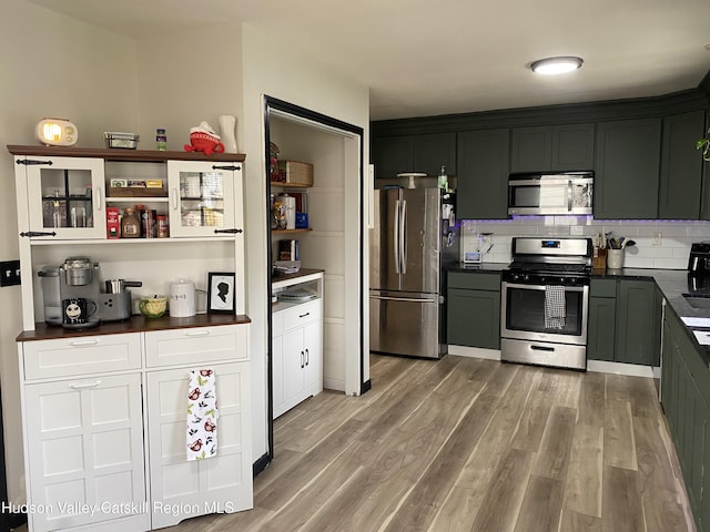 kitchen featuring open shelves, dark countertops, light wood-type flooring, backsplash, and stainless steel appliances