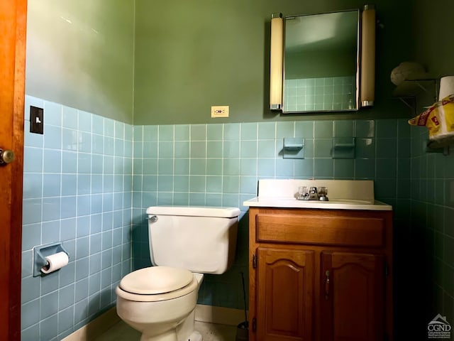 half bath with tile walls, toilet, vanity, wainscoting, and tile patterned floors