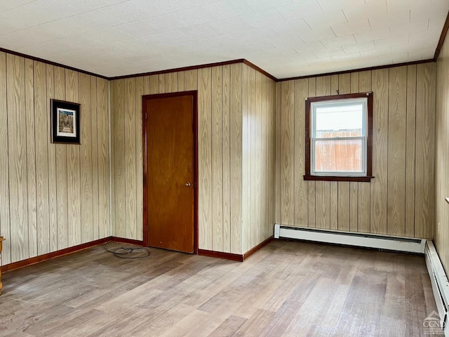 unfurnished room featuring wood finished floors, a baseboard radiator, crown molding, and baseboards