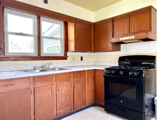 kitchen with black range with gas stovetop, a sink, under cabinet range hood, light countertops, and brown cabinets