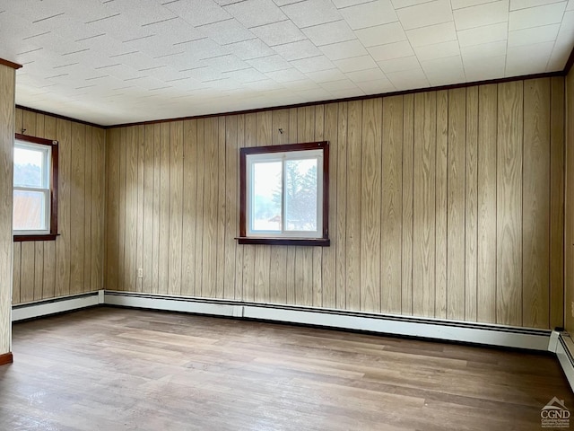 empty room with wood finished floors, wooden walls, and a baseboard heating unit