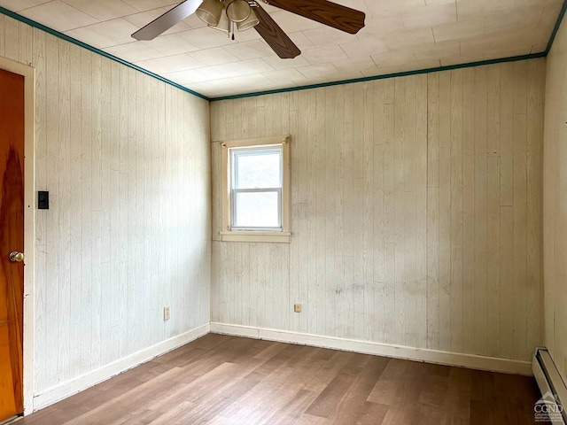 unfurnished room featuring baseboard heating, wood finished floors, a ceiling fan, wood walls, and baseboards
