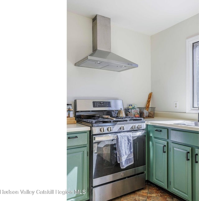 kitchen featuring stainless steel gas stove, wall chimney exhaust hood, light countertops, and green cabinetry