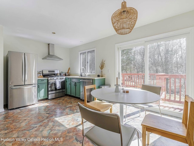 kitchen featuring green cabinetry, appliances with stainless steel finishes, light countertops, wall chimney range hood, and a sink