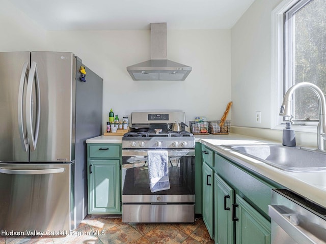 kitchen with stainless steel appliances, light countertops, a sink, wall chimney range hood, and green cabinetry