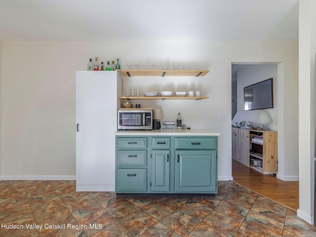 kitchen with stone finish flooring, baseboards, light countertops, open shelves, and stainless steel microwave