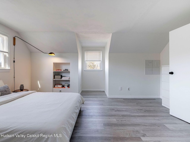 bedroom with multiple windows, vaulted ceiling, baseboards, and wood finished floors