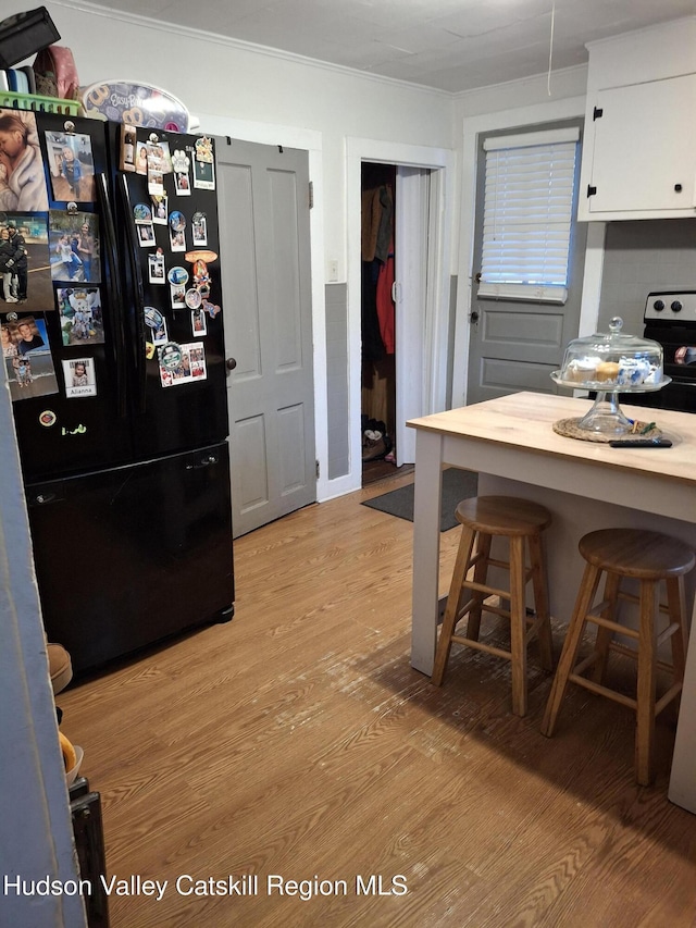 kitchen with a breakfast bar, white cabinets, ornamental molding, freestanding refrigerator, and light wood finished floors