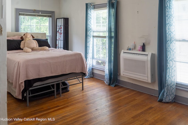 bedroom with a wall mounted AC, hardwood / wood-style flooring, and multiple windows