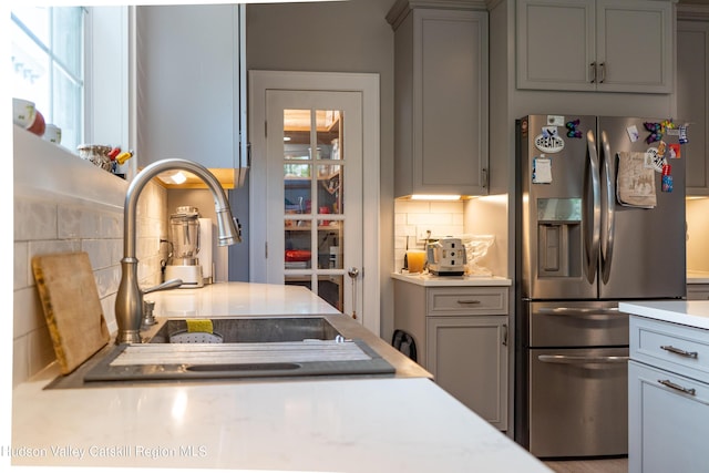 kitchen featuring stainless steel refrigerator with ice dispenser, tasteful backsplash, gray cabinets, and sink