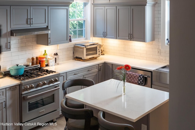 kitchen featuring stainless steel stove, decorative backsplash, gray cabinets, kitchen peninsula, and a breakfast bar area