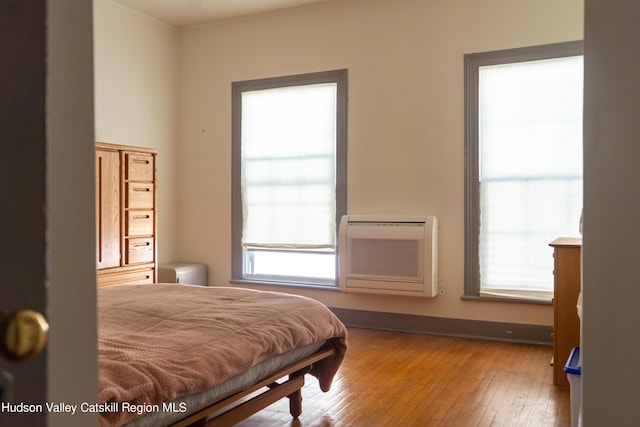 bedroom featuring a wall mounted air conditioner, wood-type flooring, and heating unit