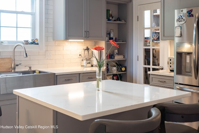 kitchen featuring stainless steel fridge, tasteful backsplash, gray cabinetry, sink, and a breakfast bar area