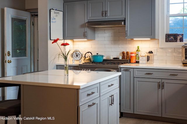 kitchen featuring a center island, light stone counters, backsplash, gray cabinets, and a breakfast bar