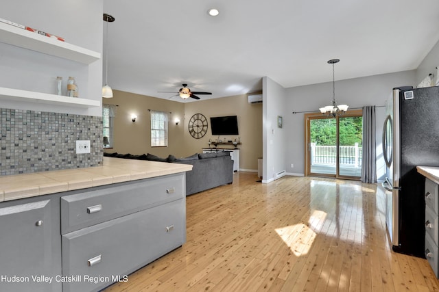 kitchen featuring backsplash, decorative light fixtures, light hardwood / wood-style flooring, tile counters, and stainless steel refrigerator