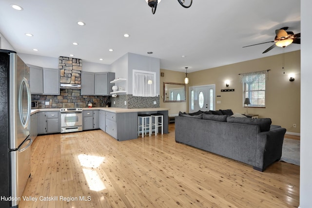 kitchen featuring gray cabinetry, ceiling fan, tasteful backsplash, light hardwood / wood-style floors, and appliances with stainless steel finishes